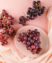 Red grapes in a plate on pink and textile background. top view.