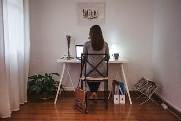 Back view of woman working on white desktop on home office.