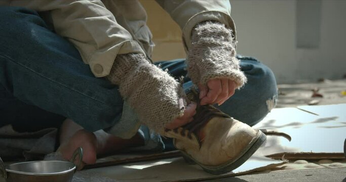 Homeless man on the sidewalk and tying shoelaces.