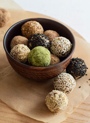 Homemade healthy vegan raw energy truffle balls in brown bowl. Made with dried dates, walnuts, almonds and cashews in sesame seeds, matcha powder and carob. The concept of healthy and vegetarian food.