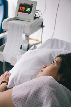 Young woman on hospital bed looking to medical equipment measuring her vital signs