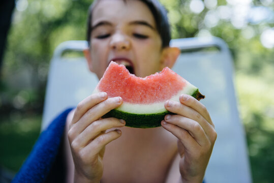 Boy takes a ravenous bite of a watermelon slice