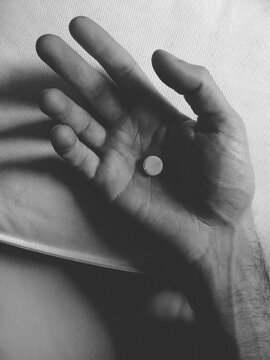 Hand of a young man holding a little pill.