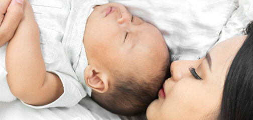 Portrait of enjoy happy love family asian mother playing with adorable little asian baby.Mom kiss with cute son moments good time in a white bedroom.Love of family concept