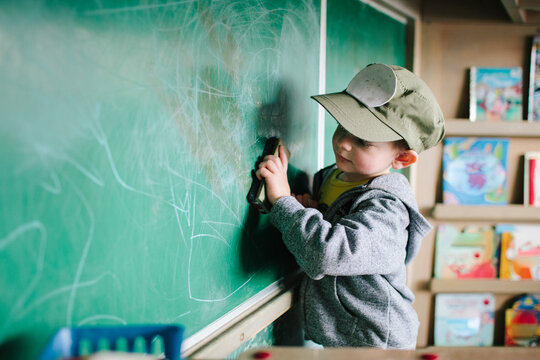 a little boy drawing on a green chalk board