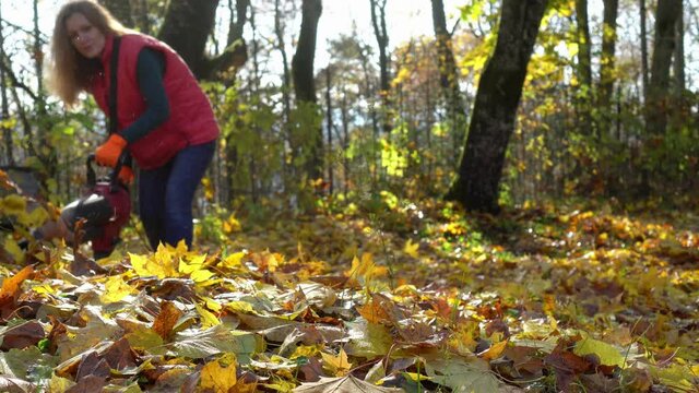 Strong gardener woman fighting autumn leaves in house backyard with leaf blower