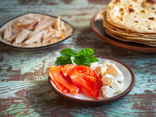 A set of products for cooking pita. Tortillas, cheese, chicken fillet and tomatoes on three plates