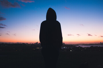 Woman with hood looking in top of the city during sunset