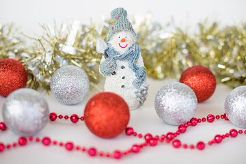 Christmas and new year decorations. Christmas composition of little snowman in hat and scarf, silver and red balls, beads and glitter garland on white background.