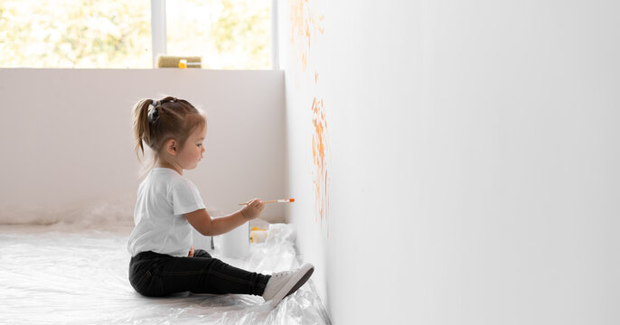 little girl with a brush in her hands draws on the wall. Home renovation concept.