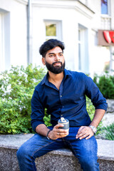 Obraz premium Young Indian man drinking coffee from reusable cup outdoors.