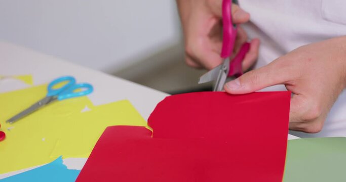 Close up of a male hands, while he is cuting with scissors an object from the coloured paper.