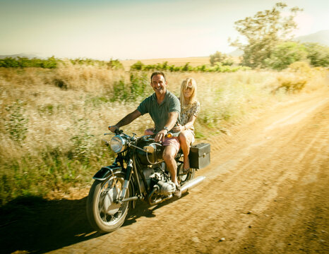 Man a woman riding a classic motorcycle on a dusty dirt road at sundown