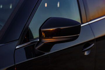 Part of the body of a black car at sunset