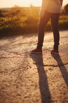 Girl with red sneakers and jeans standing on the road at sunset