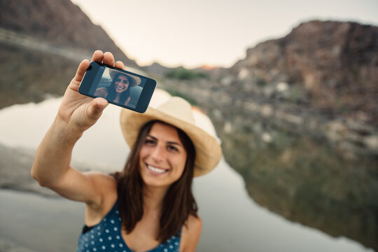 Attractive woman wearing a hat taking a selfie near a lake or river