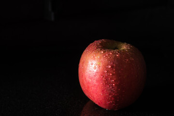 Red apple covered in water drops on black background. Health Concept with refreshing fruit.