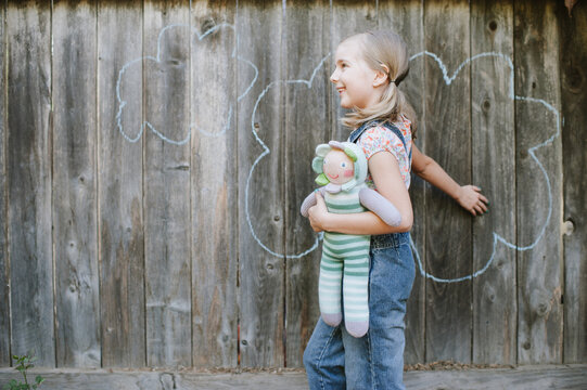 young girl playing with doll on a rustic fense