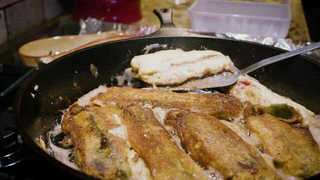 Frying chile rellenos in a cast iron skillet. The delicious cheese stuffed green peppers are a staple of Southwestern New Mexican cuisine.
