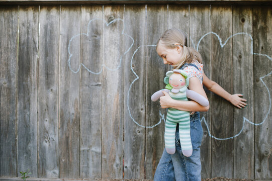 young girl playing with doll on a rustic fense