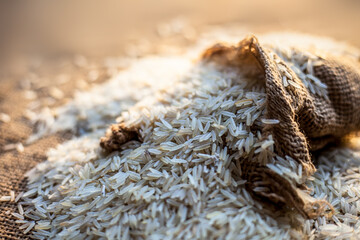 Close up shot of Raw Basmati white rice in a gunny bag on brown surface.