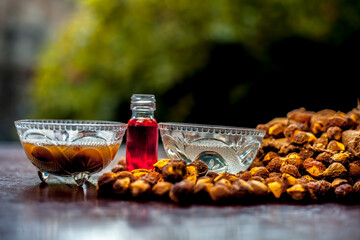 Close up shot of all-purpose homemade cleaner consisting of areetha or soapnut, essential oil, and some water. Shot of raw areetha, a bottle of essential oil on brown surface with blurred background.