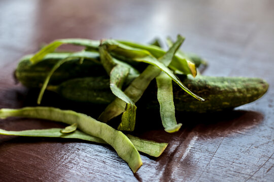 close up shot of raw Galka or sponge gourd on a brown colored wooden surface. Along with some of its peeled skin on top of it.
