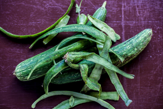 close up shot of raw Galka or sponge gourd on a brown colored wooden surface. Along with some of its peeled skin on top of it.