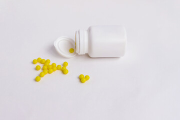 Yellow round pills are poured out of a white bottle on a white background. Medicinal form of dragees.