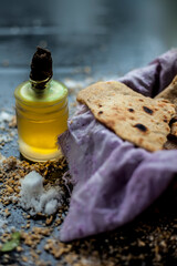 Shot of bhakri in a basket container along with some wheat flour spread on the surface and some cooking oil in a small glass bottle on a black colored surface. 