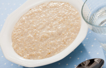 White plate with cooked oat porridge on blue textile background. Healthy diet breakfast