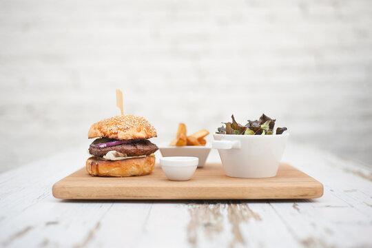 Premium hamburger with salad, french fries on a wooden plate and agains rustic white background.