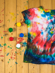 A paint-stained wooden table with a tie dye t-shirt. Flat lay.