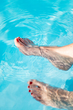 Conceptual photograph of some feet testing the pool water.