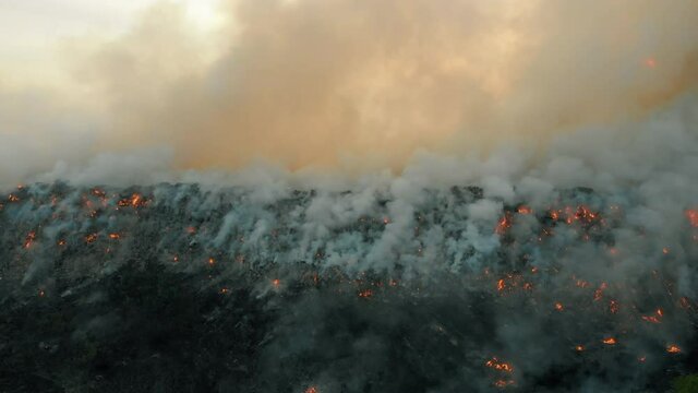 Aerial view at fire at garbage dump, burning pollutes the environment. Ecological catastrophe and destruction of nature, large fire area, camera moves into the distance