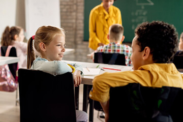 Obraz na płótnie Canvas Smiling girl talking to her classmate in the classroom.