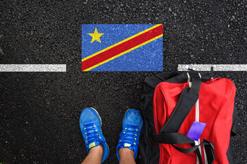 a man with a shoes and travel bag is standing on asphalt next to flag of DR Congo and border 