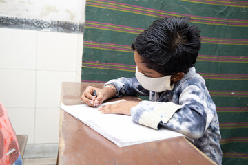 Fototapeta na wymiar Indian boys student studying In classroom wearing mask maintaining social distancing looks at camera, school reopen during covid19 pandemic, new normal. 
