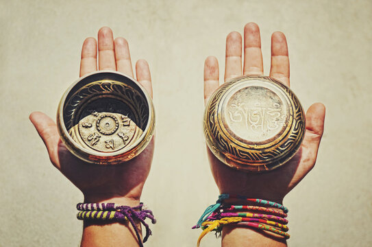 Two (2) hands holding and showing both sides of decorated Tibetan Singing Bowls