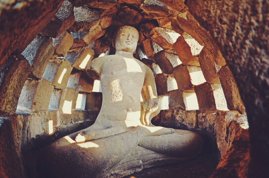 Statue of a stone Buddha in a sitting meditative lotus position inside the Borobudur, Indonesia