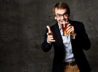 Middle-aged man in stylish official clothing jacket and shirt holds a glass of drink craft beer and points finger at camera