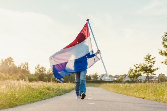 Boy walking a long road holding a Dutch flag in the sunlight