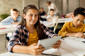 Happy schoolgirl using digital tablet during a class in the classroom.