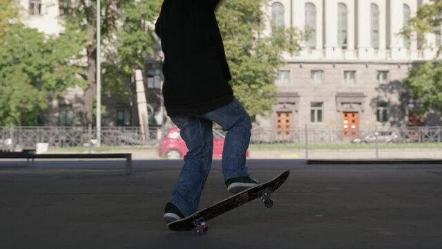 Professional skateboarder guy in dark clothing performs an trick on skateboard. Teenager rides on back wheels of skateboard performing balance tricks on site of skate Park under an iron bridge.