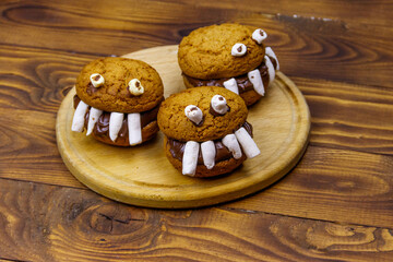 Halloween dessert: Toothed monsters made of oatmeal cookies, chocolate spread and marshmallows on a wooden table