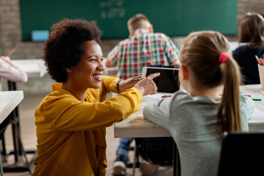 Happy black teacher and schoolgirl using digital tablet in the classroom.