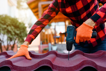 Close up of contractor hands in protective gloves are drilling with electric drill a metal tile...