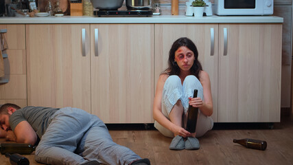 Wife drinking alcohol near drunk husband looking desolated at him. Traumatised abused terrified...
