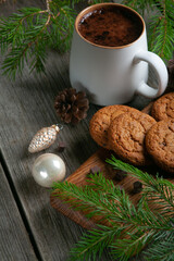 Happy New Year composition. Christmas still life made of fir branches, white cup of cocoa, oatmeal cookies with chocolate and pink toys on a rustic black wooden background.