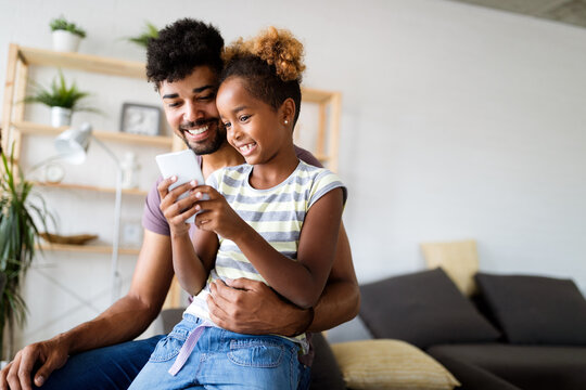 Happy father and daughter having fun with smartphone, smiling at funny video, playing mobile game